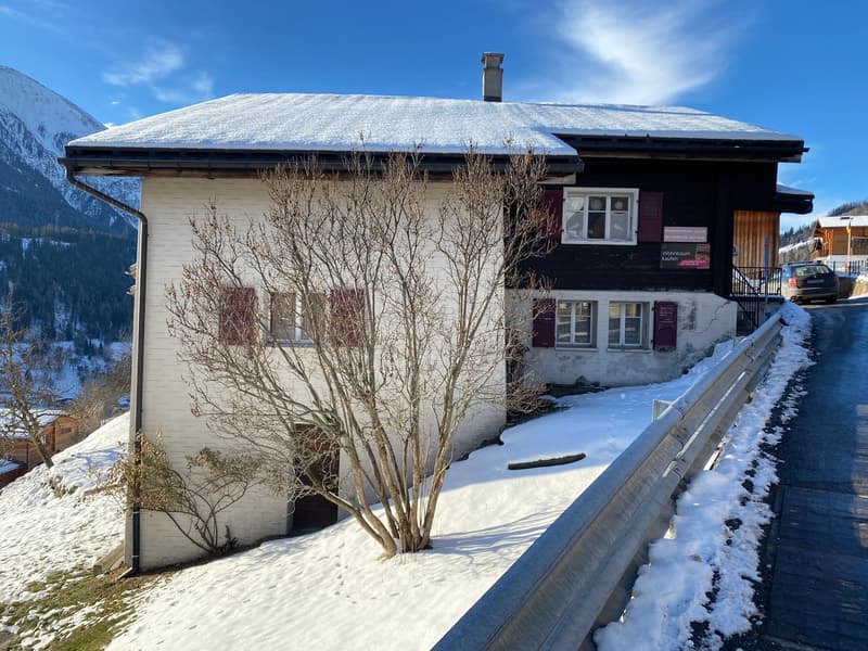 2 story house, white and black facade, snow-covered roof, chimney, red shutters, car parked in front, snowy mountain background