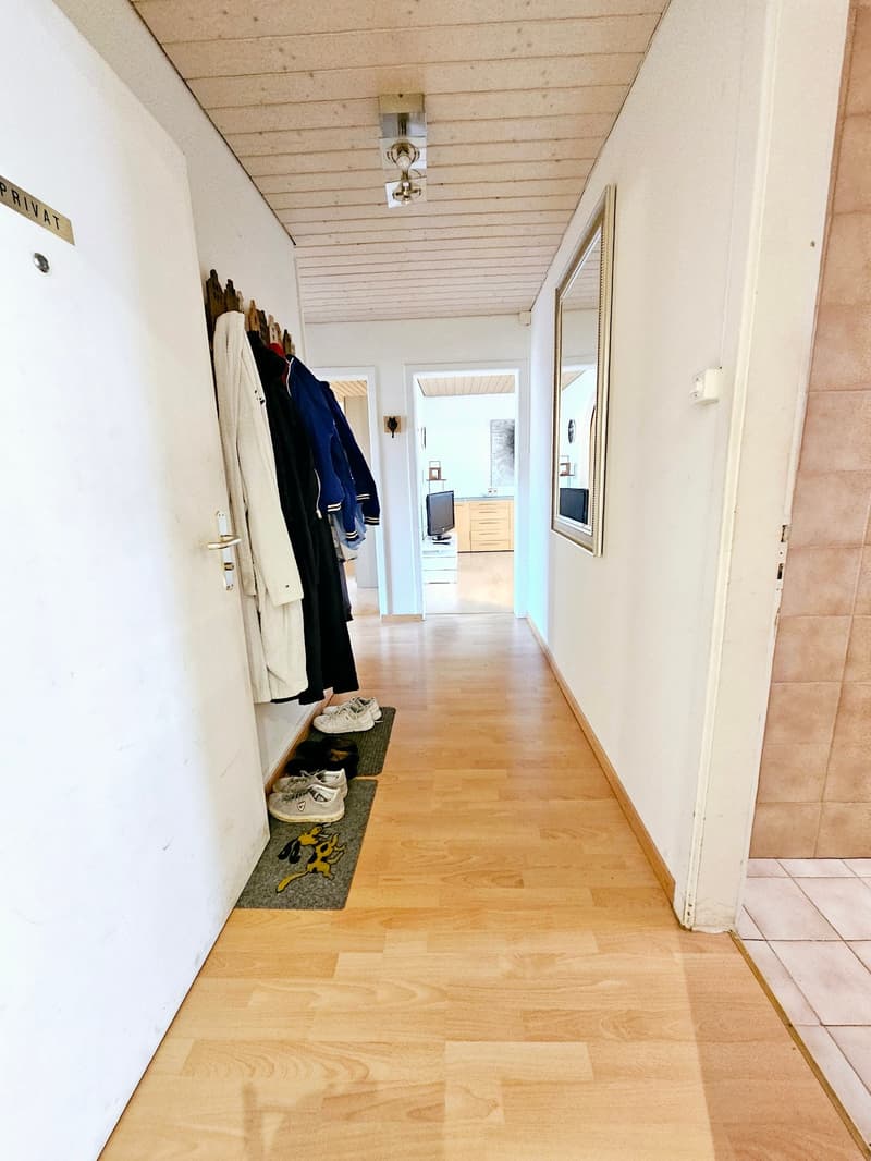 Wooden floor, white walls, wooden ceiling, coat rack with clothes, private washing machine, mirror