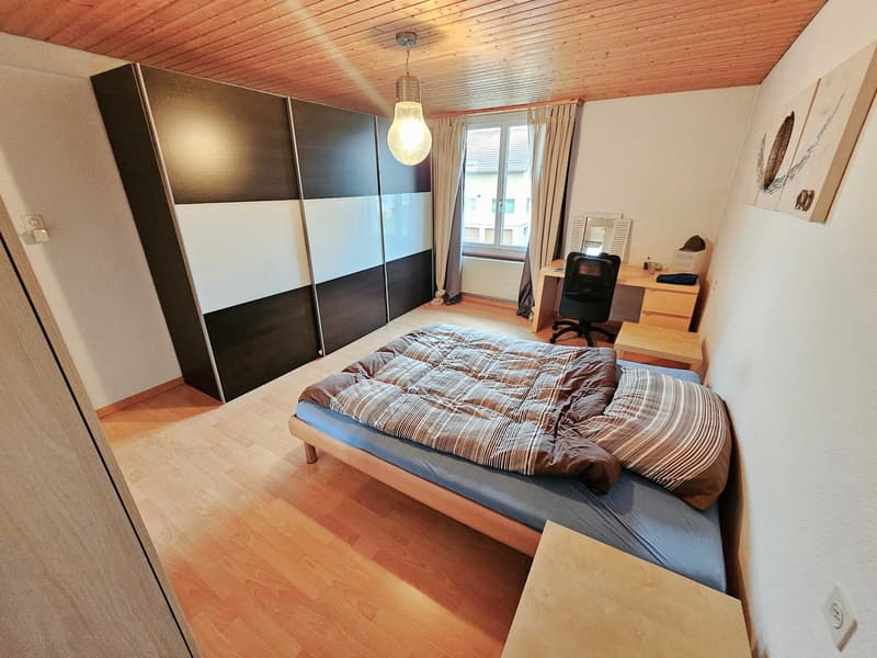 Bedroom with wooden ceiling, large sliding wardrobe, bed with patterned bedding, desk, and a window