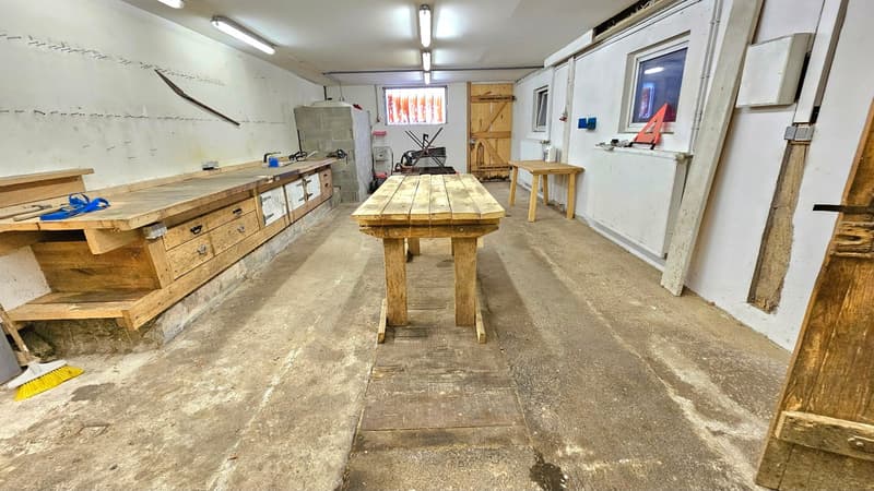 Large space, workshop, several wooden workbenches, storage boxes, tools, concrete floor, bright lights on ceiling