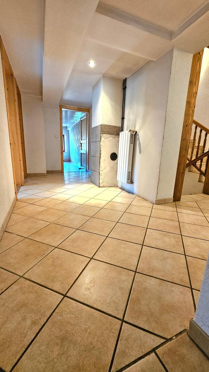 a hallway with wooden flooring and walls, white ceiling with ceiling light, a radiator attached to the wall, a wooden staircase, and a doorway leading to another room.