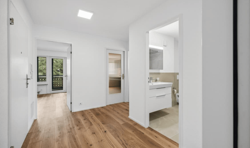 Modern bathroom with glass doors, white fixtures, wooden floor