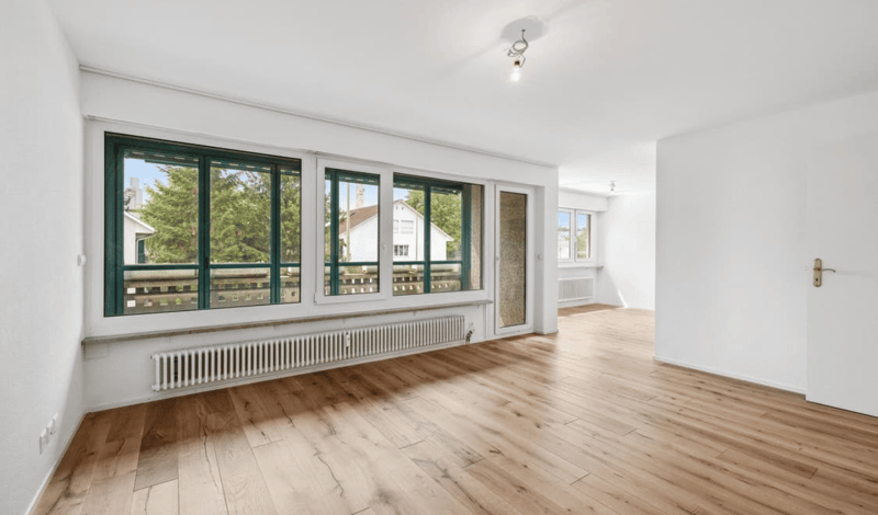 large wooden floor, white walls, wide windows with green frames, balcony