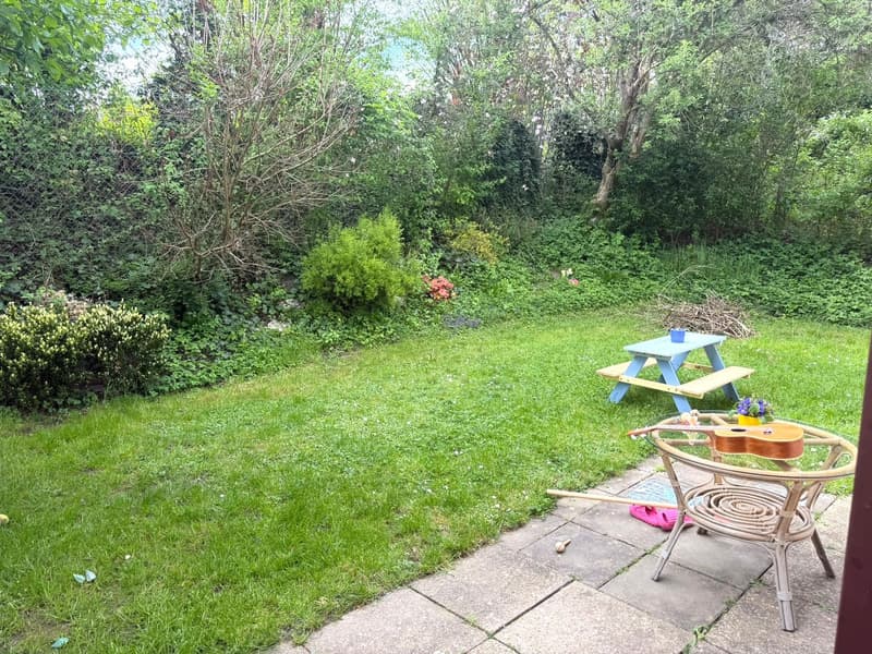 A garden with a wooden bench, a blue table, a guitar on a table, and a grassy area.