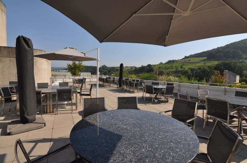 Restaurant on the roof with view on the mountains, several tables, chairs, and umbrellas.