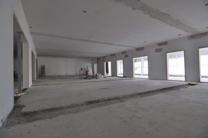 An empty room with large windows, a smooth concrete floor, a few construction materials and tools are present