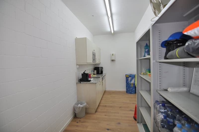 A small storage area with a kitchen setup, includes cabinets, counter, coffee machine, and storage shelves.