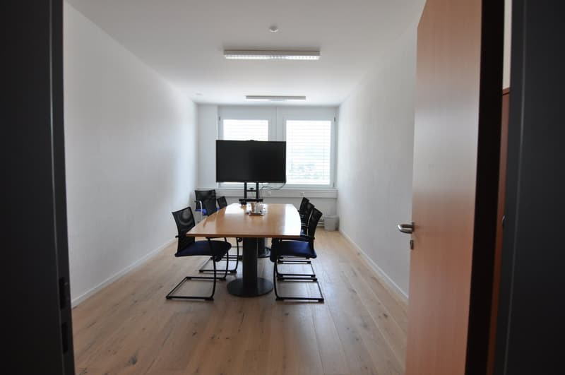 Empty conference room with a table, chairs, and a TV monitor on a stand in front of a window
