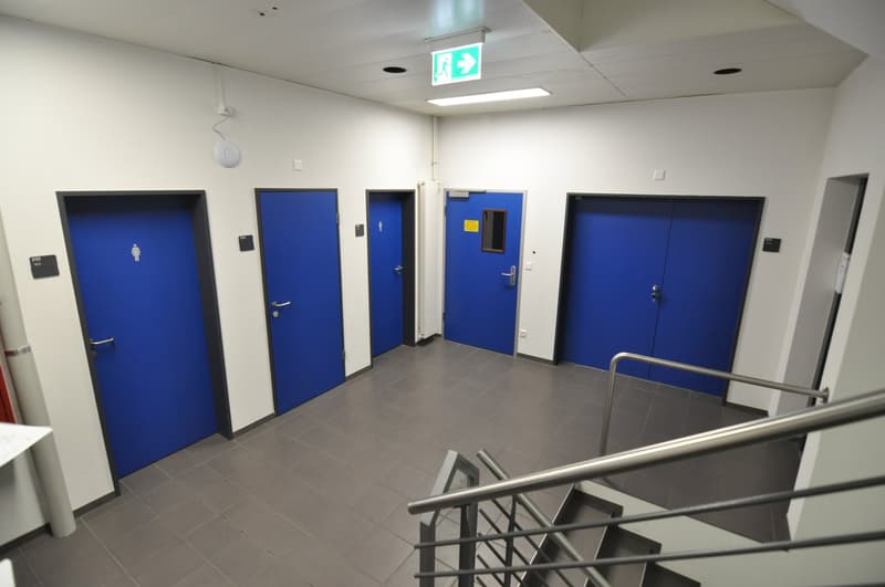 Corridor with blue doors and tiled floor, emergency exit sign, steel handrails on staircase