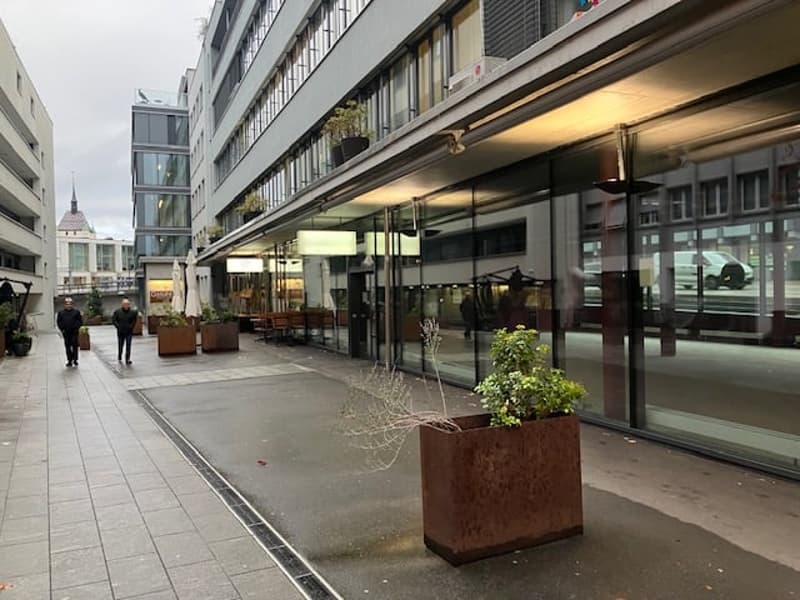 modern building with glass walls, large windows, potted plants on the side, people walking in front