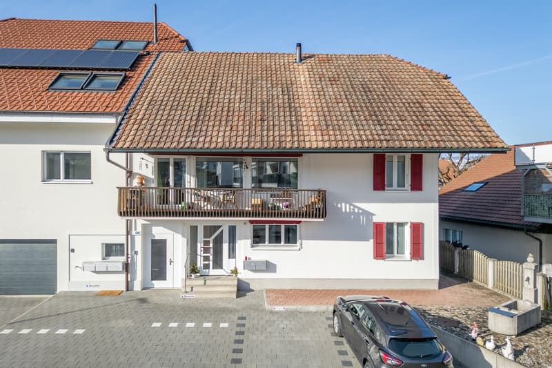 Two-story house, white paint, red roof, solar panels, red shutters, balcony, attached garage, driveway