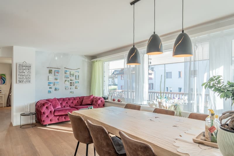 dining area with a wooden table and red sofa, large windows with a view to the balcony