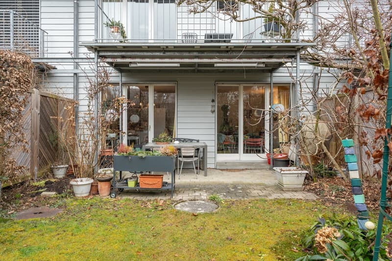 Outdoor dining area with table, chairs, balcony, garden, metal structure, potted plants, and grass.
