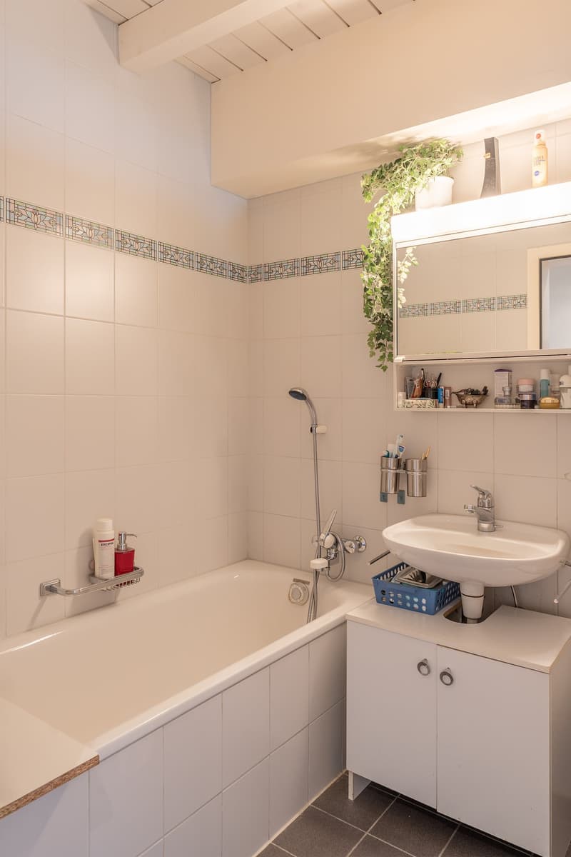 white tiles, bathtub, sink, showerhead, mirror with shelf, under-sink storage, soap dispenser