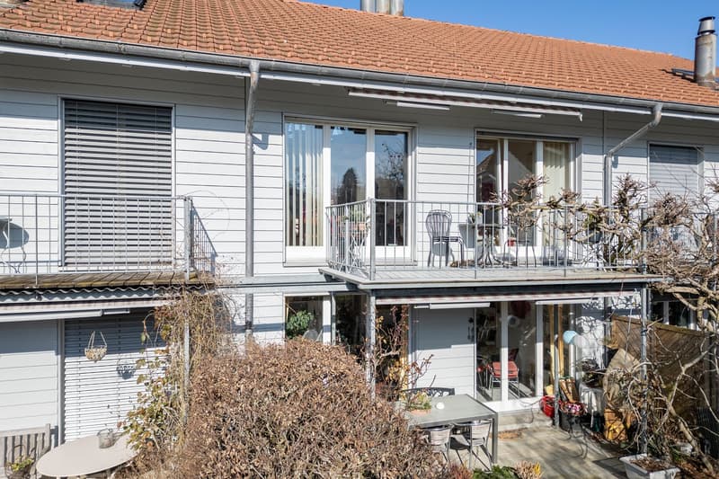 3 story white house with red roof, terrace, large windows, plants and shrubs