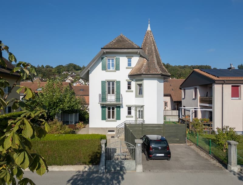 3 story house, white exterior, green shutters, brown roof, car parked in driveway, green fence, garden