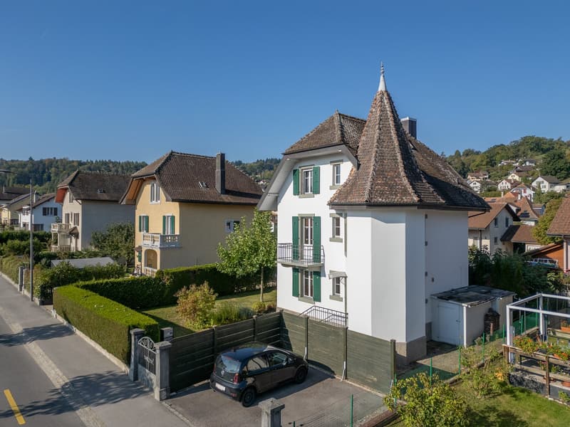 3 story house, white exterior, brown roof, green shutters, car parked in front, garden, hedges, neighboring houses