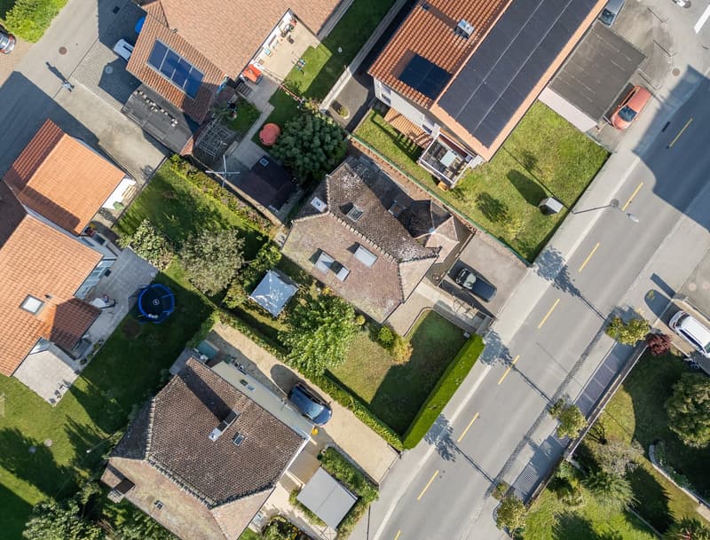 Aerial view of a neighborhood with several houses, each with a garage, solar panels on the roofs, and cars parked in front.
