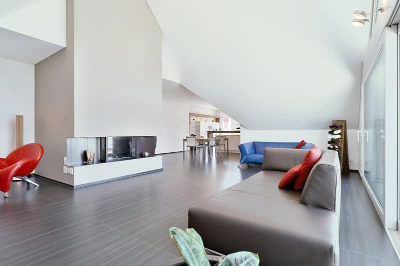 Fireplace, hardwood floor, grey sofa with red cushions, table with chairs, red chair, large windows