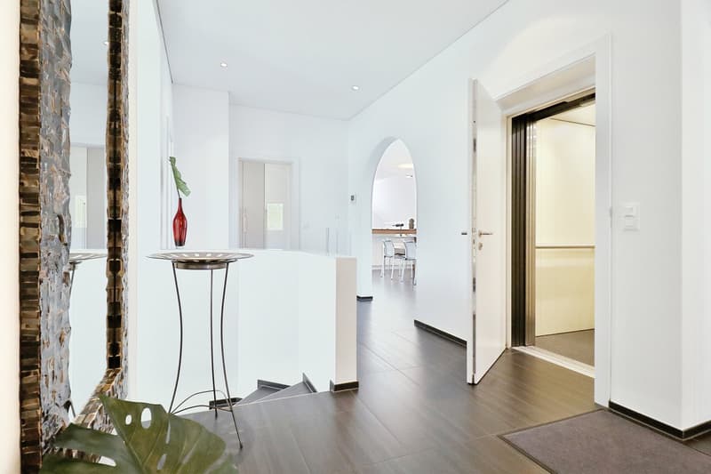 white walls, wooden floor, open door to elevator, a table with a plant, a mirror