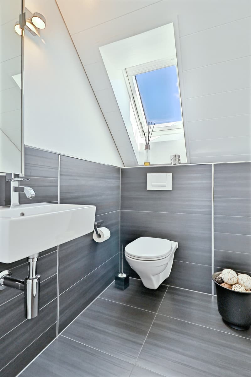 modern bathroom with white sink, toilet, mirror, skylight, and grey tiles