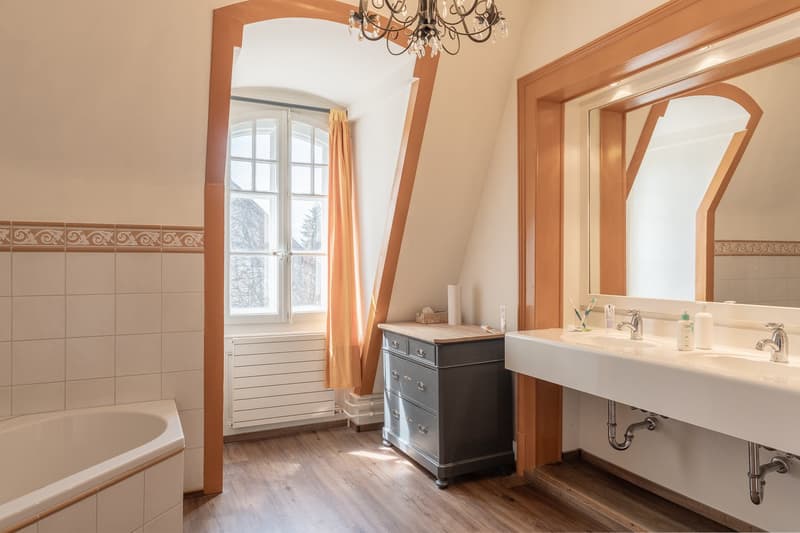 Bathroom with bathtub, double sink, mirror, wooden floor, window, radiator, cabinet, chandelier