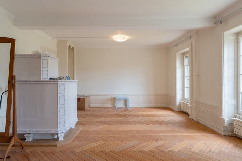 Empty room with wooden parquet floor, white walls, a white cabinet, a small blue table, and a mirror.