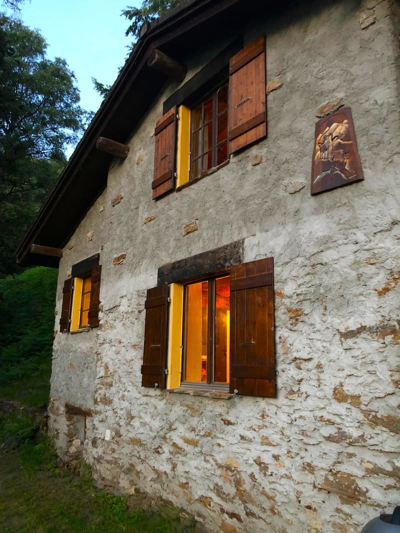 Old stone house with wooden shutters, balcony, and a decorative wall panel