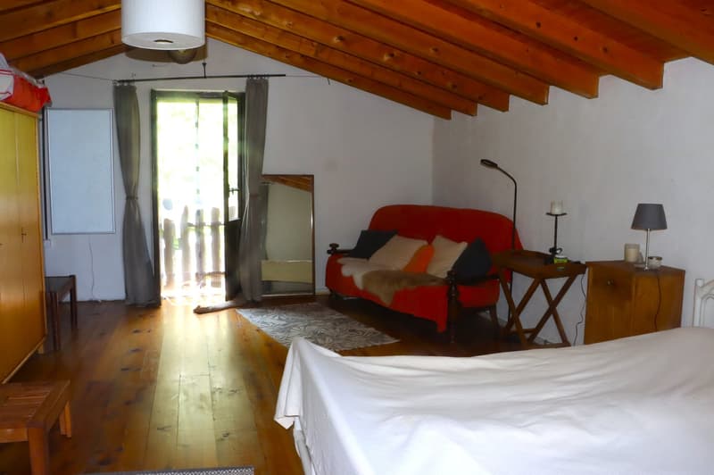 Cozy bedroom with wooden ceiling beams, a red sofa, a side table, and a balcony door leading to a balcony or terrace