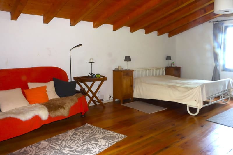 Spacious bedroom with wooden ceiling beams, red sofa, wooden side table, dresser, and a hospital bed