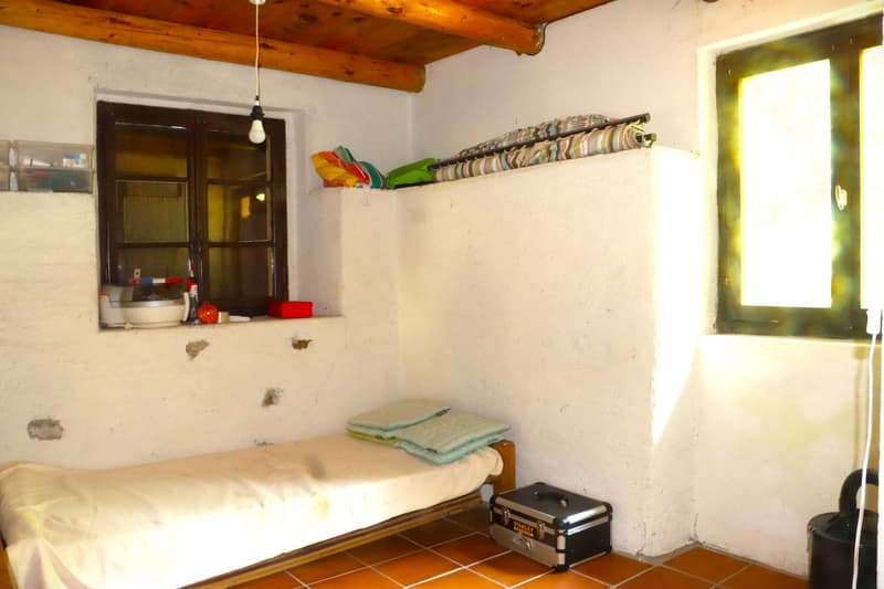 Rustic bedroom with wooden ceiling beams, single bed, shelving unit, and storage boxes