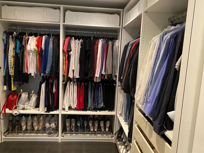 A spacious walk-in closet with white shelves, a metal bar for shoes, hanging clothes, and a shelf for handbags.