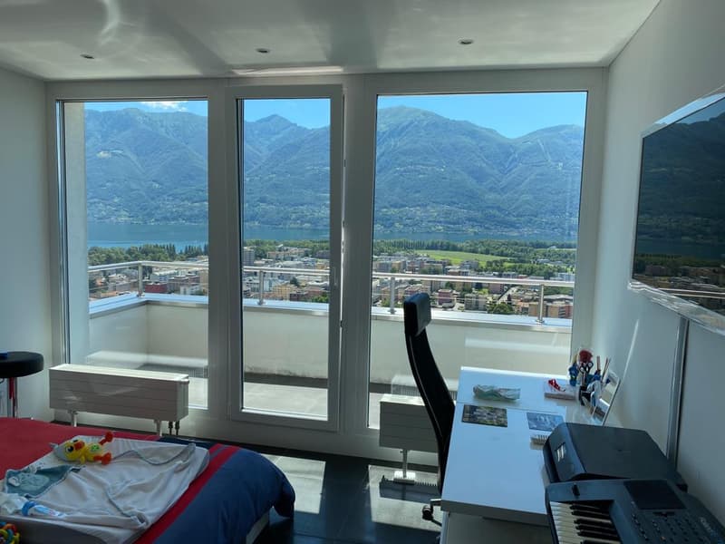 bedroom with bed, table, chair, piano, desk, large windows with balcony