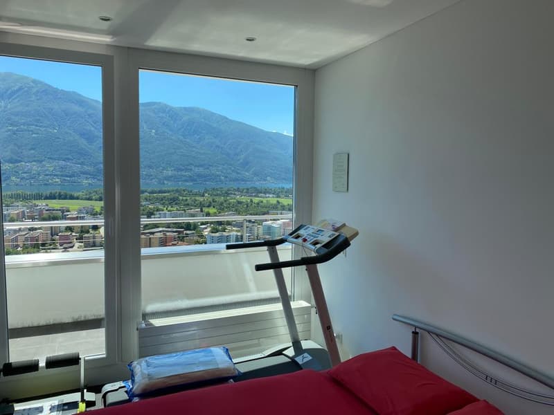 a treadmill, a bed, red pillows, a balcony with mountain view
