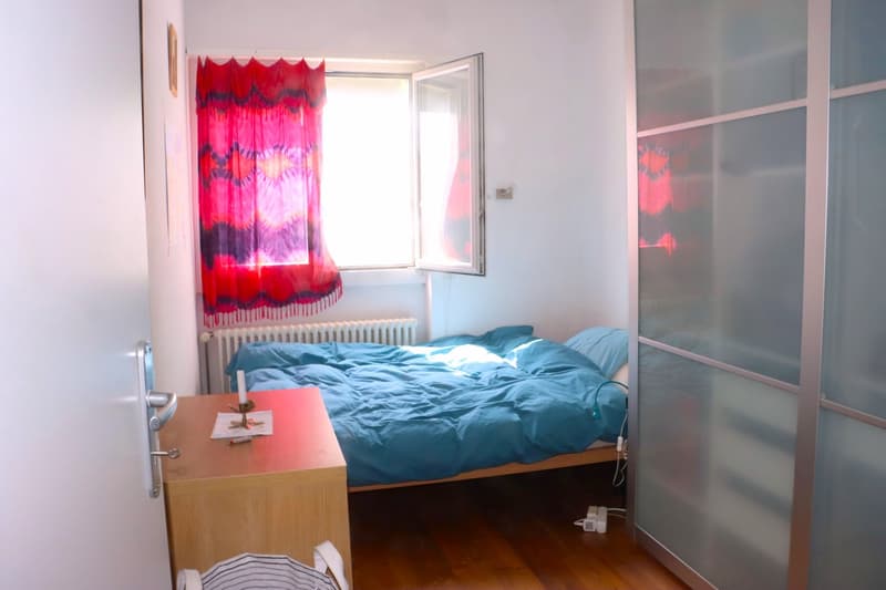 small bedroom with bed, nightstand, and window with red curtain