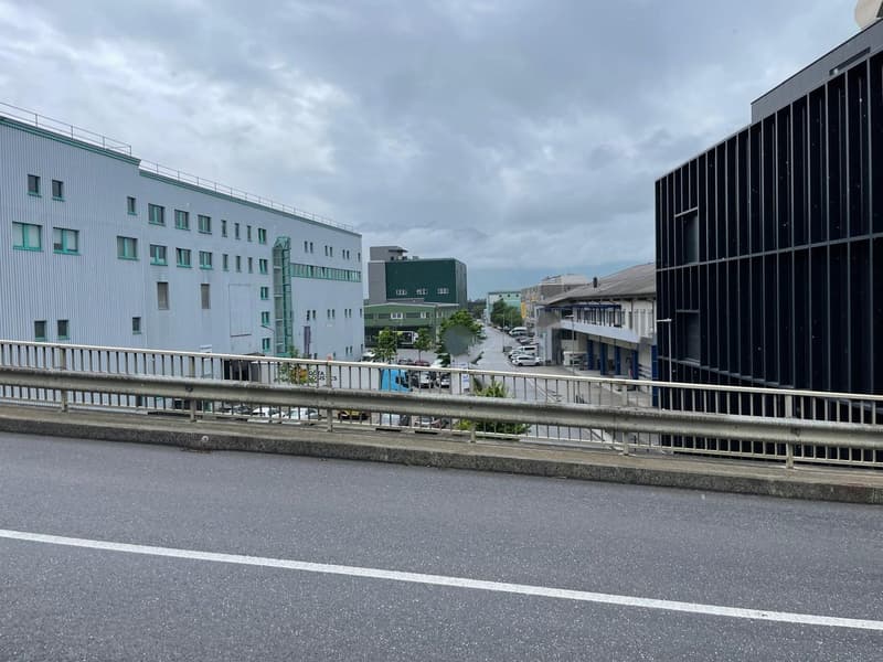 Bridge with metal guardrails, cars on the street, buildings on both sides, cloudy sky