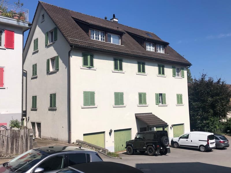 3 story house, white walls, brown roof, green shutters, 2 garages