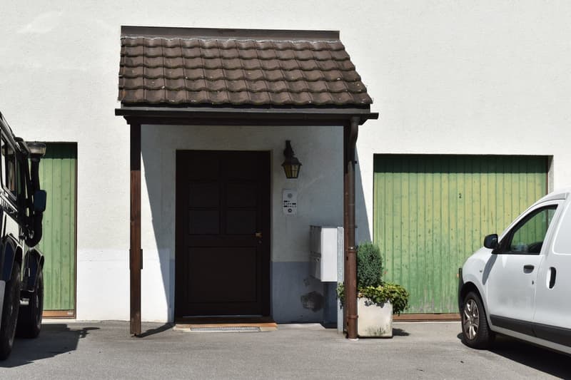 white house, brown door, green garage doors, mailbox, plant, cars parked