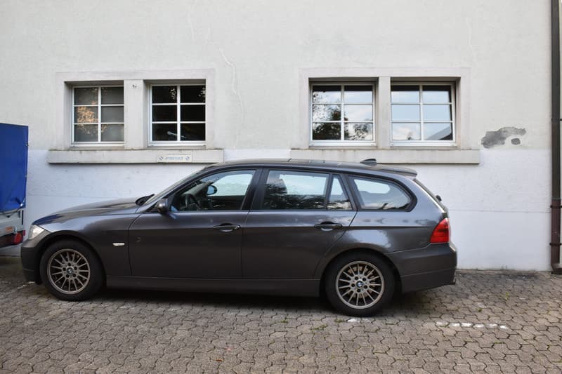 Gray BMW 3 series wagon parked in front of a white building with two windows