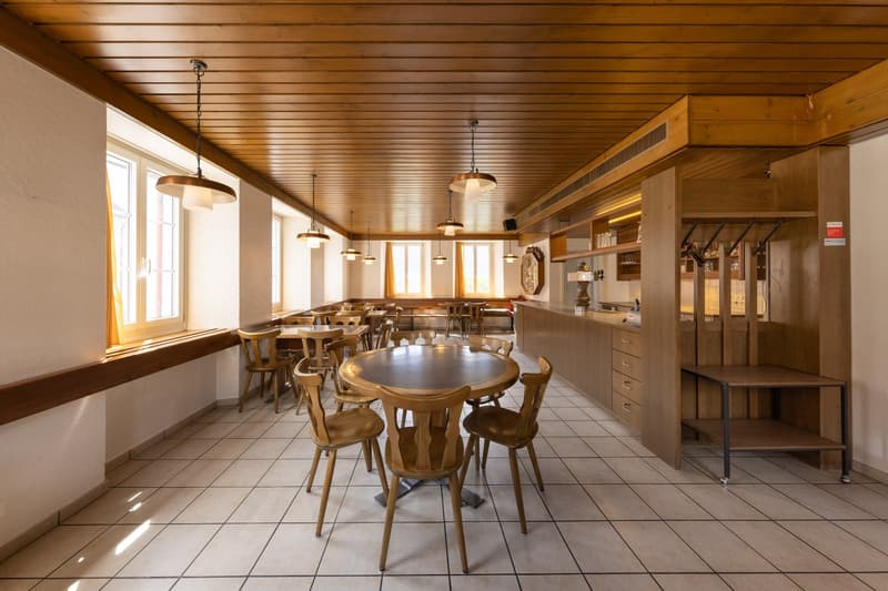 Large open-plan kitchen and dining room with wooden ceiling, tile flooring, round wooden dining table with chairs, pendant lighting, and a kitchen counter with appliances including a dishwasher.