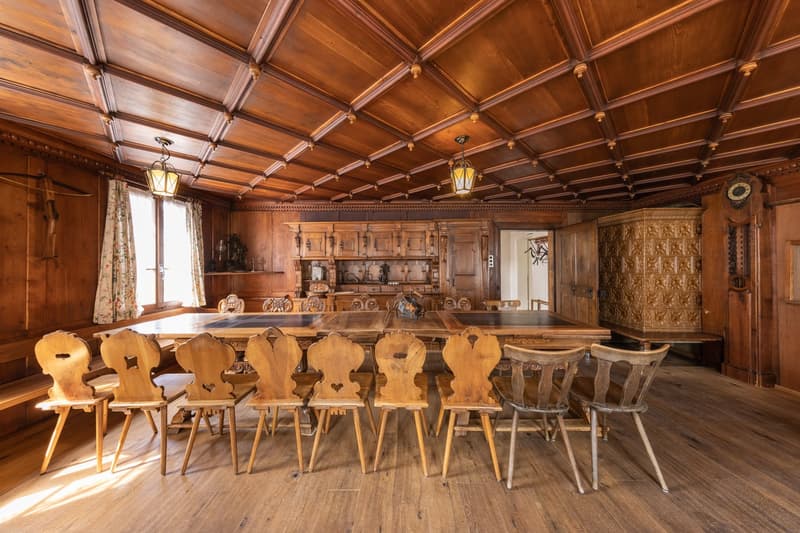 Large wooden dining room with ornate wooden ceiling, wooden chairs and table, wooden cabinets and shelves, and decorative lanterns hanging from the ceiling.