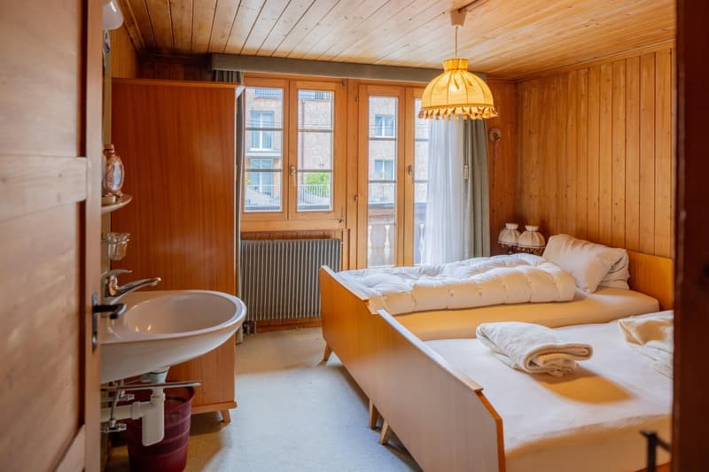 Cozy wooden bedroom with large windows, a double bed, a sink, and a decorative lamp fixture