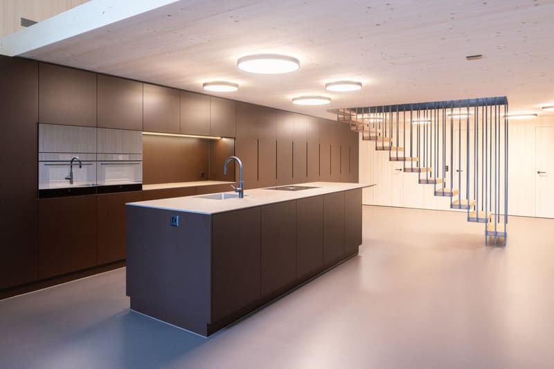 Modern kitchen with wooden floor, central island, integrated appliances, minimalist design, overhead lighting, open layout