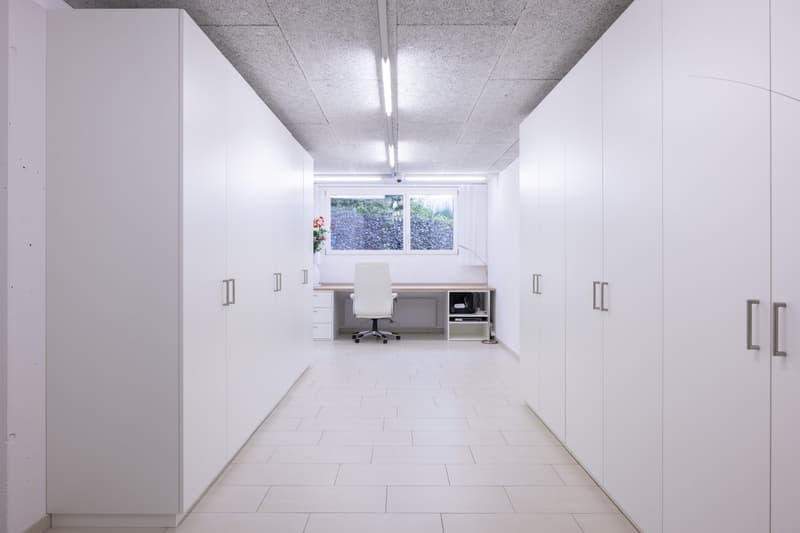 Spacious office with white walls, built-in storage cabinets, a desk with a computer, and a window overlooking the outdoors.