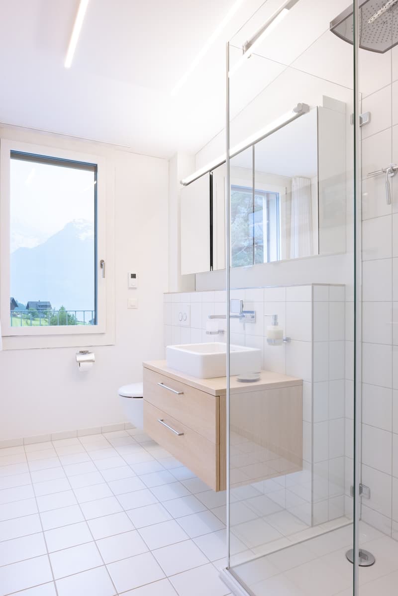 Spacious bathroom with large window, white tiles, vanity unit with vessel sink, and glass shower enclosure