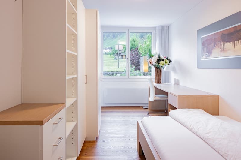 Spacious bedroom with large windows overlooking a scenic outdoor view, built-in wardrobe, desk, and floral decor