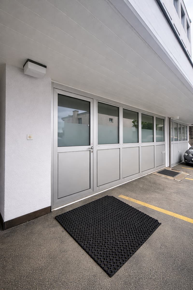 white exterior wall, glass doors, black rubber mat, parking spot