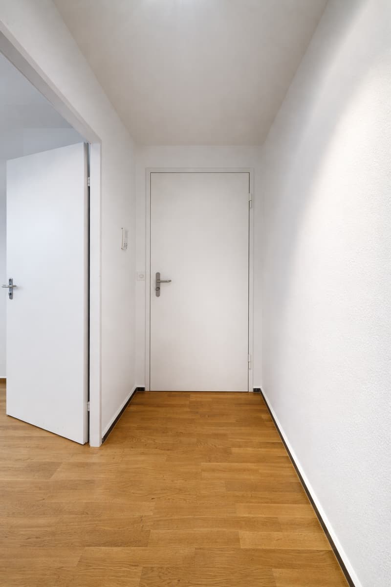 Empty room with white walls, wooden floor, two white doors, one open, one closed