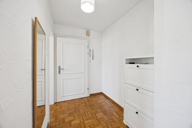 Empty hallway with white walls, wooden floor, a white door, and a mirror