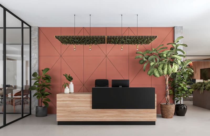 Reception area with wooden desk, black chairs, monitors, plants, and a geometric wall design.
